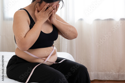 Overweight Women stressing over fat belly, using measuring tape. Overweight Woman Measuring Waist. Fat woman with tape measure, she uses her hand to squeeze the excess fat, surprise obese female. photo