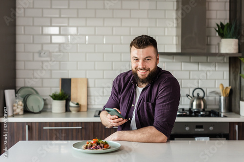 Happy Man using Smartphone App Food Delivery and eating Dinner at Home in Modern Kitchen  Portrait  Copy Space
