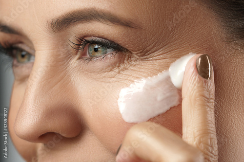 Middle aged woman applying anti-aging cream on her face photo