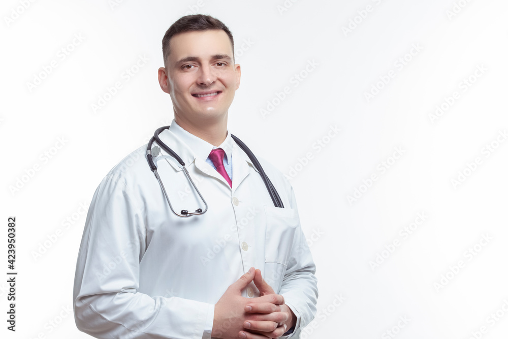 Medical Ideas. Portrait of Smiling Professional GP Doctor Posing in Doctor's Smock With Endoscope and Hands Folded in Front on White. Medical Ideas. Portrait of Smiling Professional GP Doctor Posing in Doctor's Smock With Endoscope and Hands Folded in Front on White.