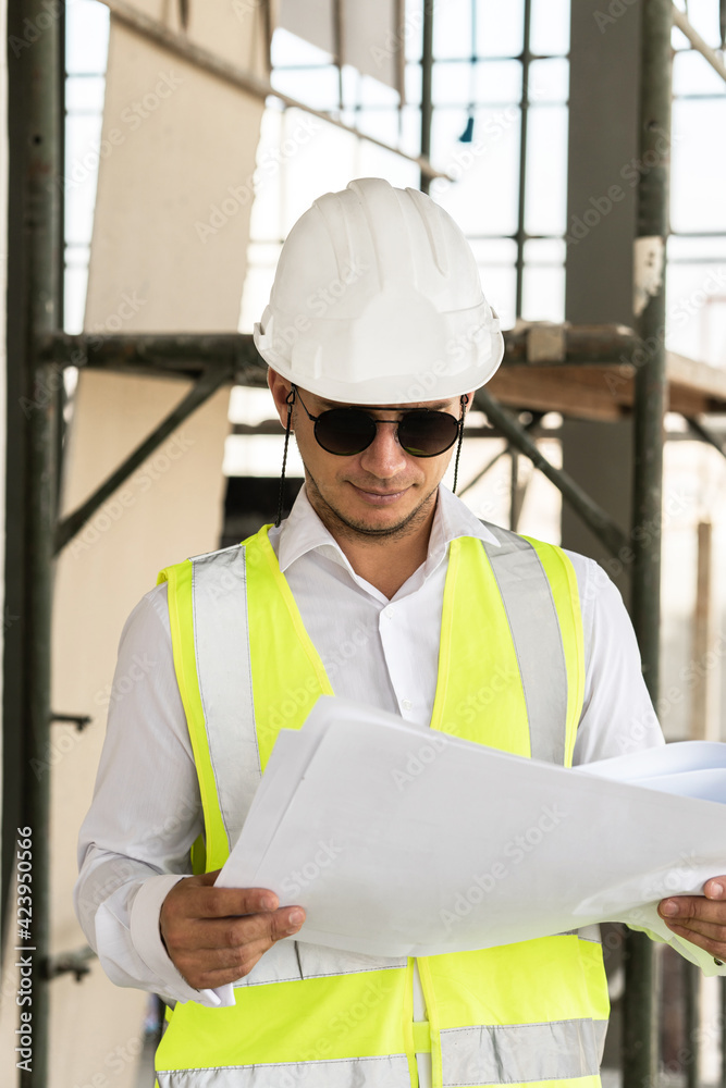 Man architect wearing safety vest with a blueprints on a construction site Man architect wearing safety vest with a blueprints on a construction site