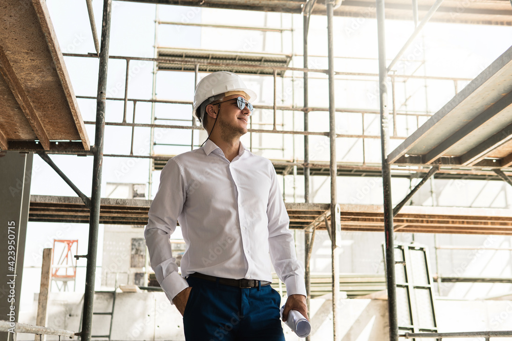 Man architect or businessman wearing hard hat and holding blueprints on a construction site Man architect or businessman wearing hard hat and holding blueprints on a construction site