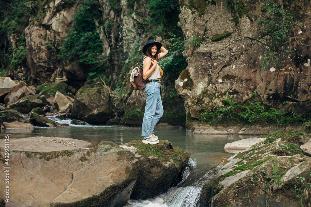 Travel and wanderlust. Stylish woman traveler with backpack relaxing at river in mountains, smiling Travel and wanderlust. Stylish woman traveler with backpack relaxing at river in mountains, smiling