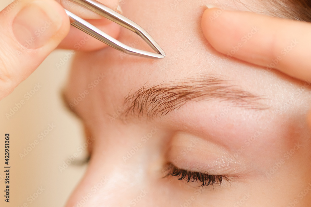 Young woman smooths her eyebrows with tweezers. Shallow depth of field