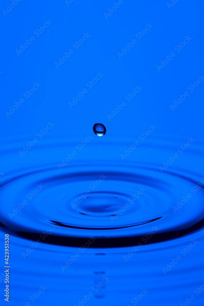 Macro Shot of One Blue Water Droplet Over Tranquil Water Surface. Macro Shot of One Blue Water Droplet Over Tranquil Water Surface.