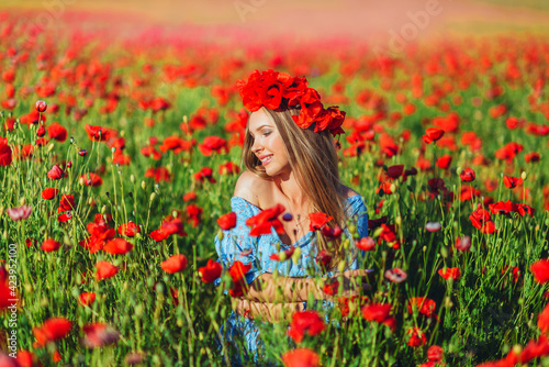 Beautiful young woman walks in a field with poppy flowers at sunset.