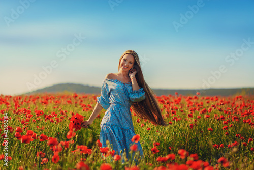 Beautiful young woman walks in a field with poppy flowers at sunset.
