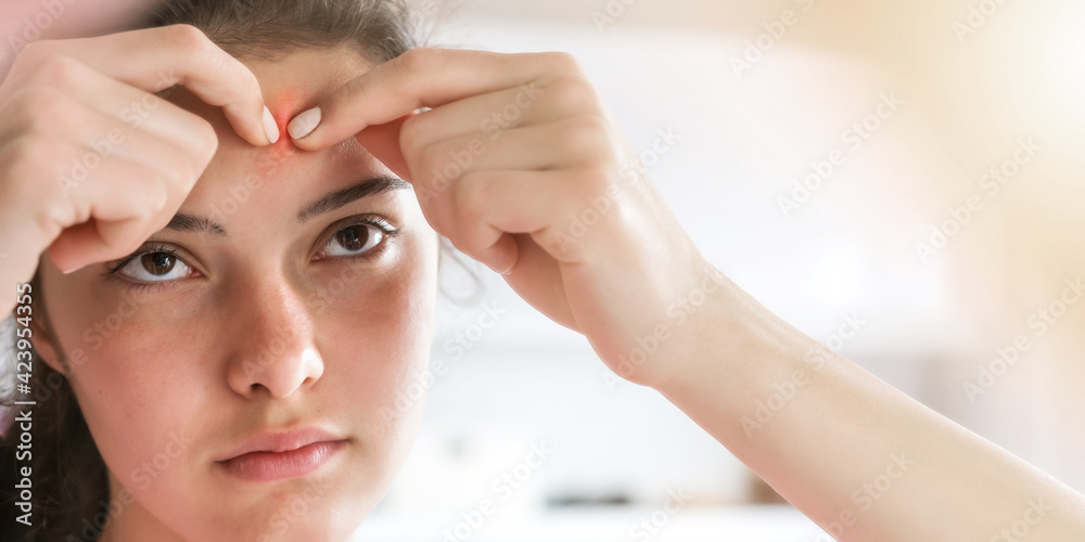 Naklejka premium teenage brunette pops zits looking at face reflection
