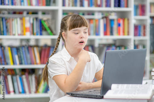 Young girl with syndrome down uses a laptop at library. Education for disabled children concept