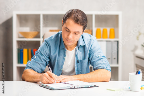 Workplace of freelance worker at home office. Young man works using pen and diary. Remote job.
