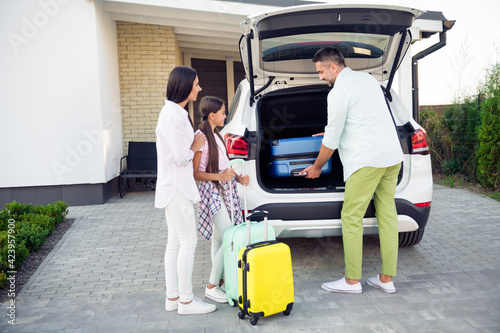 Full size photo of happy smiling family prepare to travel summer holiday father put luggage into automobile outside outdoor