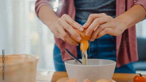 Hands of young Asian woman chef cracking eggs into ceramic bowl cooking omelette with vegetables on wooden board on kitchen table in house. Lifestyle healthy eating and traditional bakery concept.