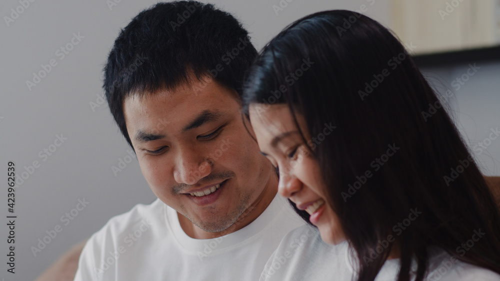 Young Asian Pregnant couple man touch his wife belly talking with his child. Mom and Dad feeling happy smiling peaceful while take care baby, pregnancy lying on sofa in living room at home concept.