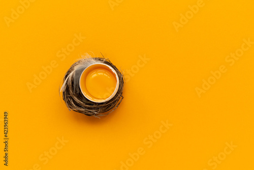 Egg yolk into nest on yellow background. Top view. Flat lay. Easter celebration