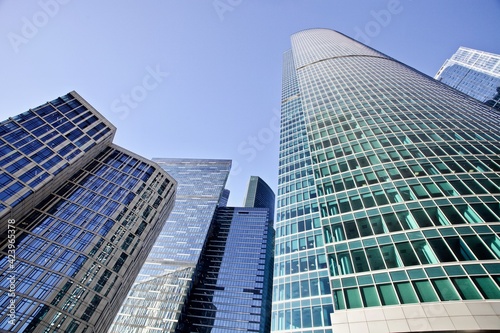Modern office buildings against bright blue sky. Bottom-up view. Glass facades of skyscrapers with contrasting highlights and reflections. Economy development  finance and business concept. Downtown.