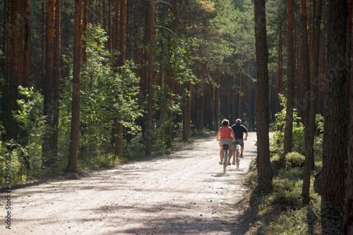 Two adults ride bicycles on a dirt forest road, view from the back © morelena