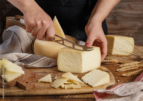Hands cut pieces of fresh homemade cheese on a wooden board