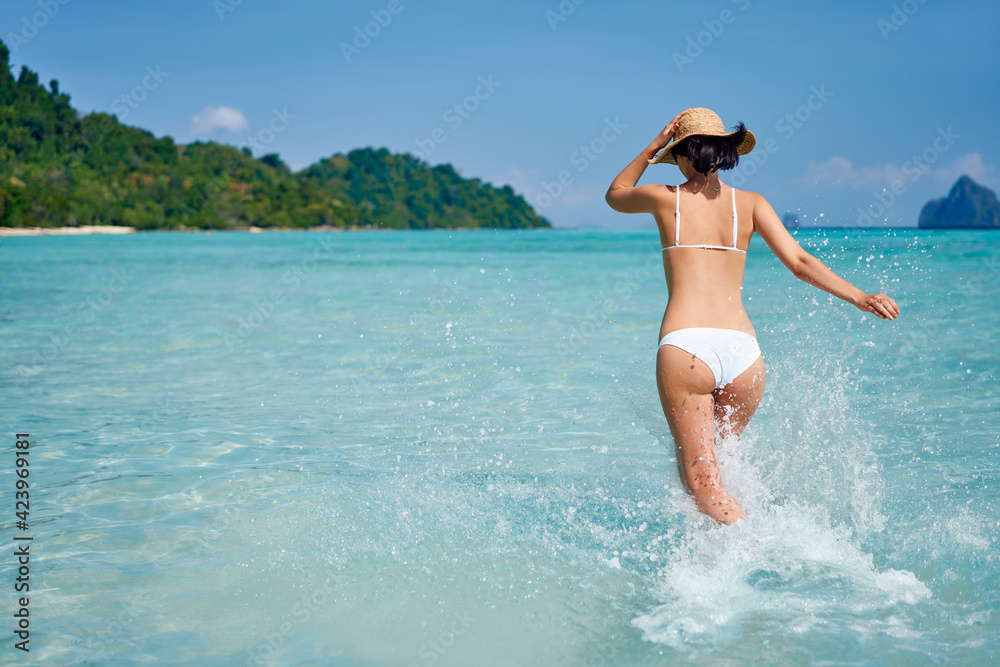 Happy slim woman running into the sea enjoy her tropical beach vacation, having fun and splashing water
