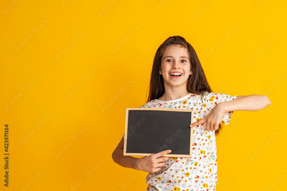 cheerful, happy teenage girl points her finger at an empty blackboard, copying the space for the text. smiling, enthusiastic teenager in bright T-shirt is showing off. Advertising concept. Copy space cheerful, happy teenage girl points her finger at an empty blackboard, copying the space for the text. smiling, enthusiastic teenager in bright T-shirt is showing off. Advertising concept. Copy space