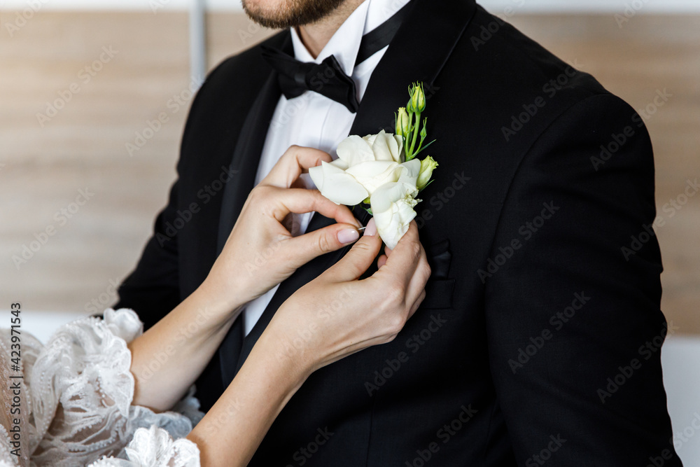 Pretty young Caucasian bride pinning a tender buttonhole bouquet to her groom's jacket