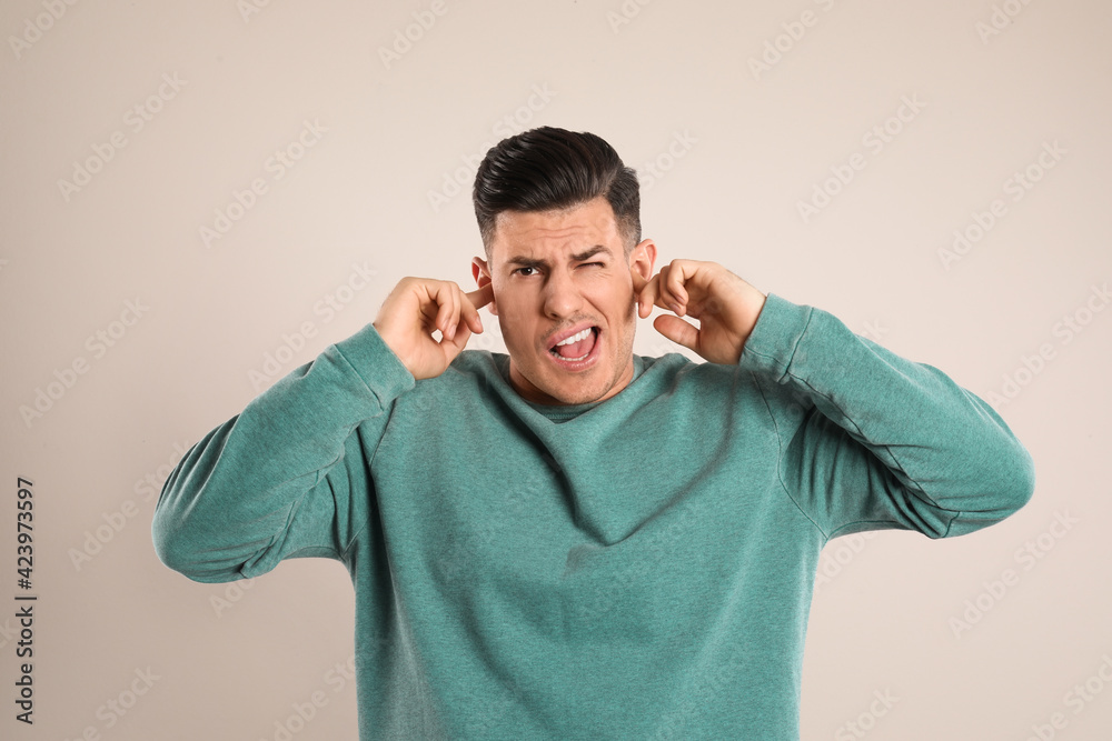 Emotional man covering ears with fingers on beige background Emotional man covering ears with fingers on beige background
