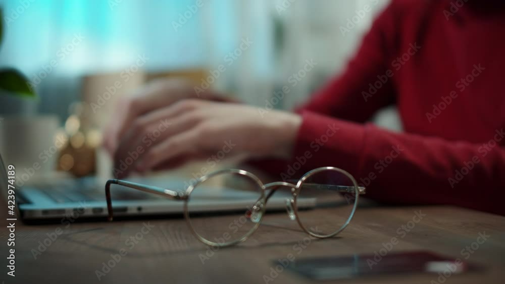 Young man is typing on laptop. Student is working on computer. Male is using online video conference for remote learning. Close-up of glasses and credit card on the table. Young man is typing on laptop. Student is working on computer. Male is using online video conference for remote learning. Close-up of glasses and credit card on the table.