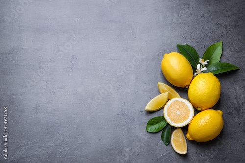 Many fresh ripe lemons with green leaves and flowers on grey table, flat lay. Space for text