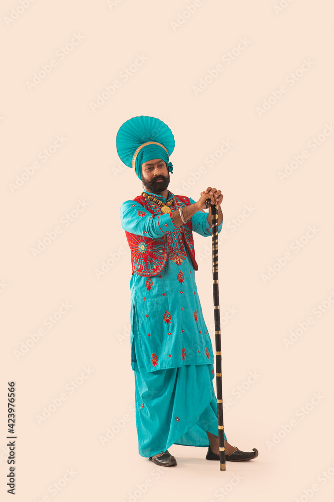 A Bhangra dancer with a grave expression standing with the Khunda.	