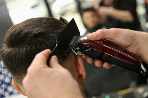 Professional barber making stylish haircut in salon, closeup