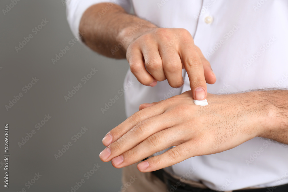 Man applying cream onto hand on grey background, closeup. Space for text Man applying cream onto hand on grey background, closeup. Space for text
