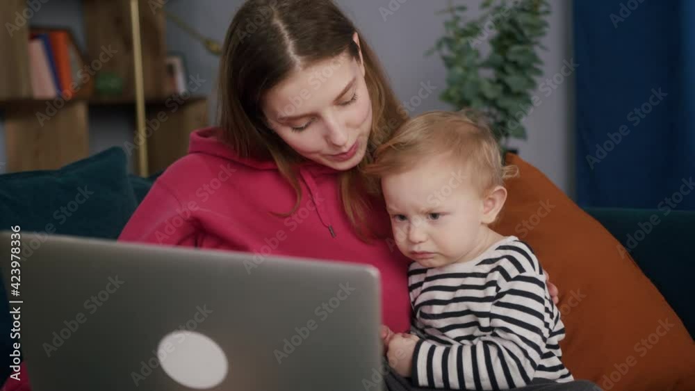Happy young mother and little son are communicating with friends online, being lockdown. Mom and child are sitting on sofa, using laptop, speaking on video chat with relatives. Happy young mother and little son are communicating with friends online, being lockdown. Mom and child are sitting on sofa, using laptop, speaking on video chat with relatives.