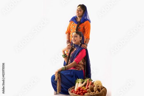 Two Women in Giddha costume together with a vegetable basket by their side.	
