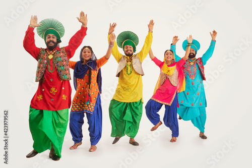 A Troupe of Punjabi Folk Dancers performing a dance step with hands up in the air.	 photo
