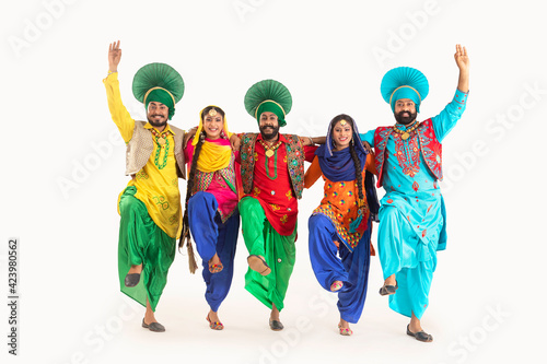 A troupe of Punjabi Folk dancers dressed in costume striking a dance step in unison.	