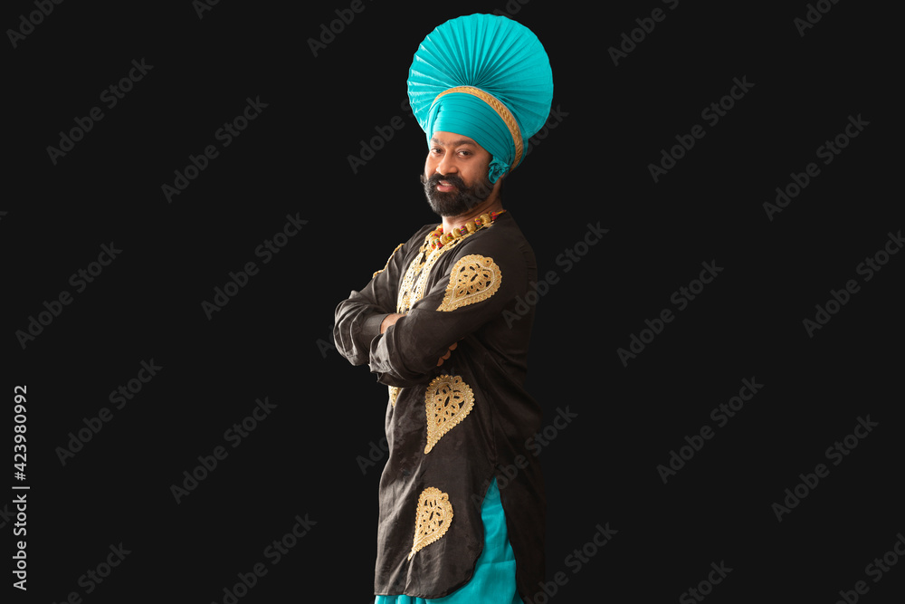 A man in Bhangra Costume smiling with his hands folded.	