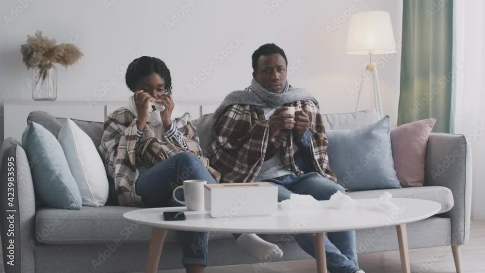 Young african american sick couple sitting on self isolation at home, feeling unwell with fever and runny nose