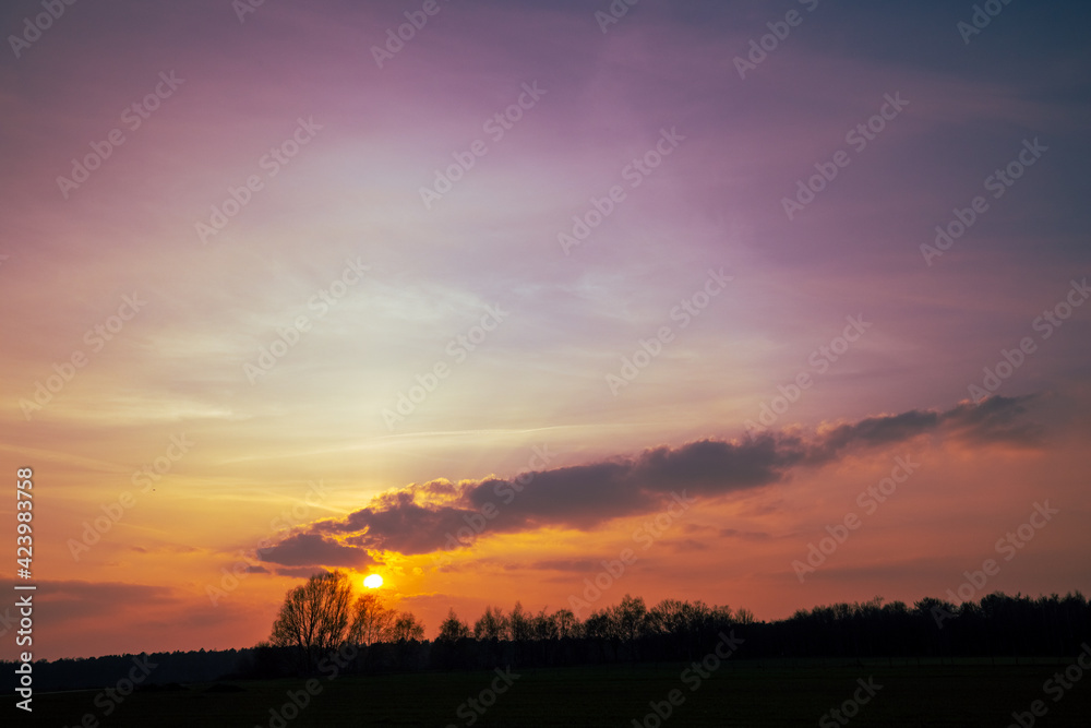 Sunset cloudy sky with picturesque clouds lit by warm sunset sunlight, colorful sunset sky with dramatic sky clouds lit by evening sunlight. Country road at sunset. High quality photo