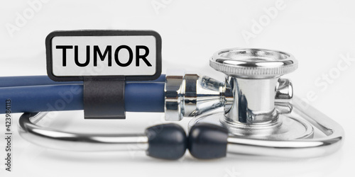 On the white surface lies a stethoscope with a plate with the inscription - TUMOR