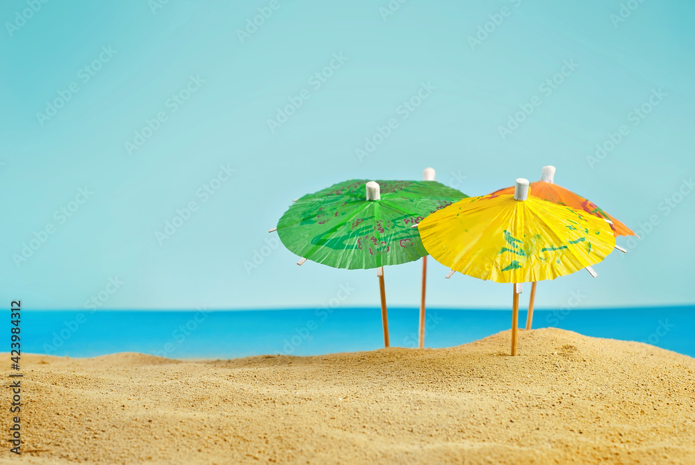 Beach umbrellas on the sand. Stylized cardboard beach. Paper umbrellas for cocktails in the background. The concept of rest, sea and vacation.