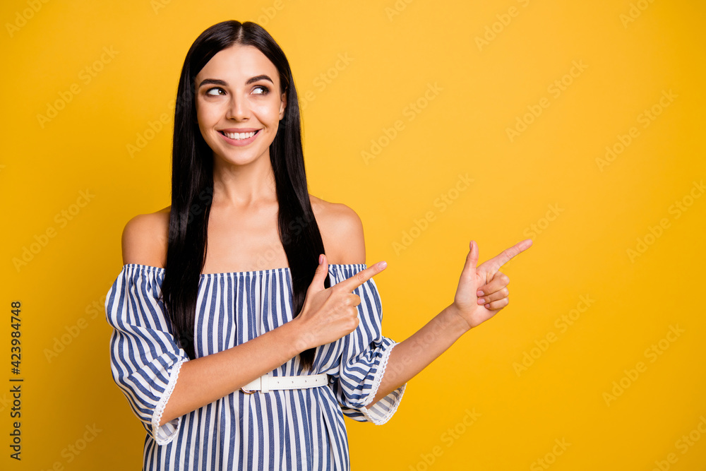 Photo of pretty shiny young lady wear striped dress pointing two fingers empty space isolated yellow color background Photo of pretty shiny young lady wear striped dress pointing two fingers empty space isolated yellow color background