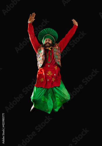 A Bhangra Dancer jumping with hands up to perform a dance step. 