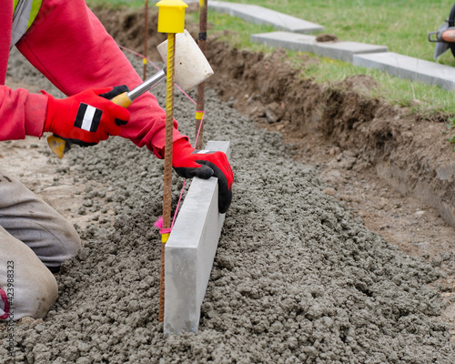 Laing edging kerb on semidry concrete during roadworks and new footpath construction  by groundworker wearing safety gloves   photo