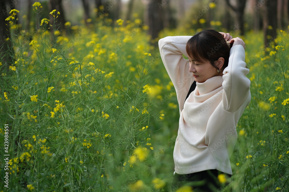 mid shot of beautiful Asian young woman fixing hair in rape flower field mid shot of beautiful Asian young woman fixing hair in rape flower field