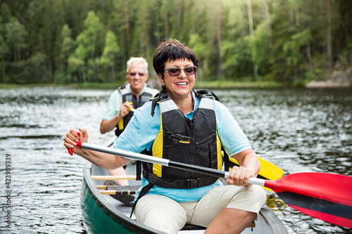 Happy mature couple in life vests canoeing in forest lake. Sunny summer day. Tourists traveling in Finland  having adventure. 