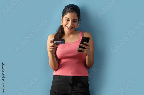A Young woman placing an order with her credit card and mobile phone. 	 photo