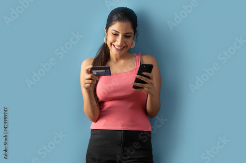 A Young woman placing an order with her credit card and mobile phone. 	