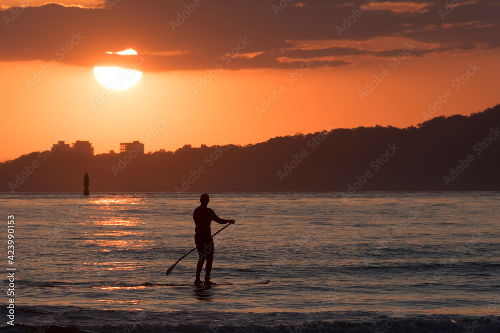 Man practicing stand up paddle in Santos city bay at sunset.