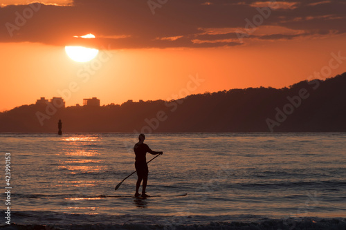Man practicing stand up paddle in Santos city bay at sunset.