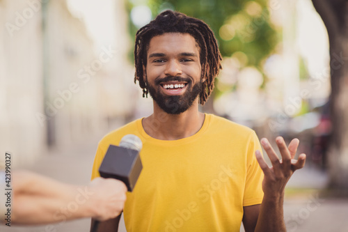 Photo portrait of young man smiling giving interview to journalist talking in microphone on street