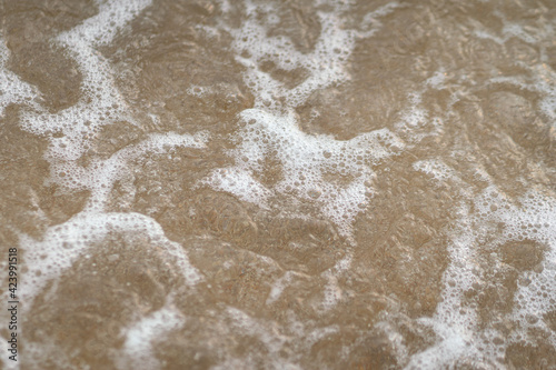 Water surface bubble of sea water after it waving with background of sand ground below. Stop motion photo, selective focus at center part.